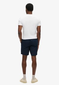 T-shirt blanche à col rond, shorts navy à pois, et baskets beiges. Les shorts sont dotés d'une taille élastique et d'un tissu doux.