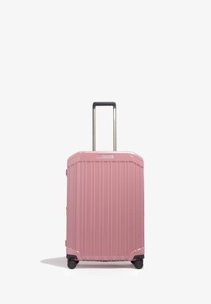 Hardcase roze koffer met verticale ribben, vier wielen en een uitgeschoven zwart handvat op een witte achtergrond.