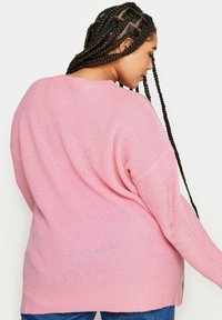 Rosa stickad tröja med lös passform, långa ärmar och sidslitsar. Har ett texturerat mönster och en bred halsringning.