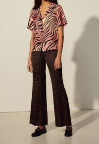 Chemise rose et noire à rayures zèbre à manches courtes associée à un pantalon large marron texturé et des chaussures noires avec des accents dorés.