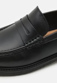 Mustad musta nahast loafer, millel on sile viimistlus, tikandid ja kummist tald. Ülemisel osal on dekoratiivne rihm vampi kohal.