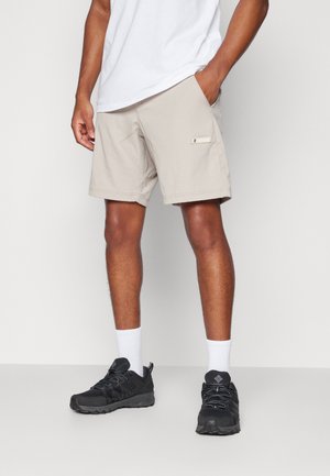 Shorts beiges en tissu léger, dotés de poches latérales et d'une étiquette logo, associés à des chaussures de sport noires et des chaussettes blanches mi-mollet.