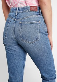 Jeans de mezclilla azul claro con un diseño ajustado, que presentan una cintura alta, bolsillos traseros y un parche de piel de la marca en la cinturilla trasera.
