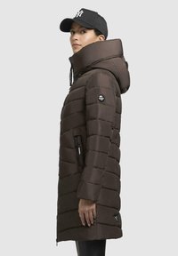 Piumino marrone con colletto alto, tasca laterale con zip e patch del logo sulla manica. Presenta una texture liscia e lucida e cappuccio.