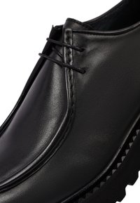 Zapato de cuero negro con una superficie lisa, detalle de costura sutil, cierre con cordones y una suela de goma gruesa y texturizada.