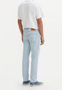 Jasnoniebieskie dżinsy z prostym krojem, z skórzaną metką na tylnej stronie pasa i dwoma tylnymi kieszeniami. Gładka biała koszulka i niebieskie trampki.