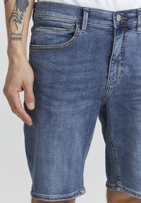 Shorts de mezclilla con un tono azul claro, diseño de cinco bolsillos y efectos de desvanecimiento suaves. Presentan un dobladillo enrollado y costuras amarillas en contraste.