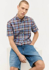 Kurzärmliges Hemd mit Knopfleiste in einem mehrfarbigen Karo-Muster in Blau, Rot und Weiß, kombiniert mit Jeansshorts.