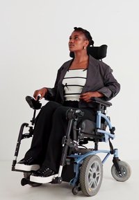 Electric wheelchair with a blue frame, black upholstery, and rubber tires. Features adjustable armrests and footrests. User wears black pants.