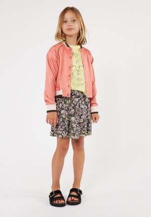 Lichtroze satijnen bomberjack, geel graphic t-shirt, zwarte bloemenrok en zwarte sandalen met gespen. Eenvoudig, kleurrijk outfitontwerp.