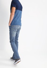 Camiseta bloqueada de color azul marino y azul claro combinada con jeans azules deslavados y zapatillas grises, mostrando un diseño de pierna recta y un ajuste casual.