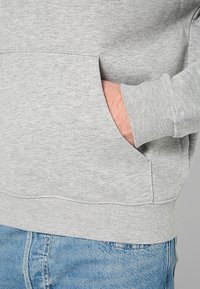 Grijze sweatshirt met een kangoeroezak, ribbelmanchetten en tailleband, gemaakt van zacht materiaal. Zichtbare stikseldetails aan de onderkant.