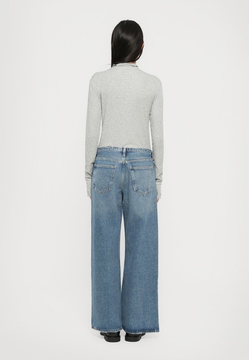 Graues Langarmoberteil kombiniert mit weit geschnittenen blauen Jeans. Die Jeans haben eine hohe Taille, fünf Taschen und eine ausgewaschene Optik. Schwarze Schuhe.