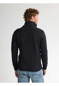Mörkgrå stickad tröja med hög ribbad krage, texturerade axlar, åtsittande ärmar och ribbad nederkant, bärs med ljusblå jeans.