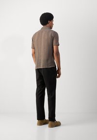 Polo tricotat maro cu mâneci scurte, având modele verticale. Asortat cu pantaloni negri și pantofi slip-on bej.