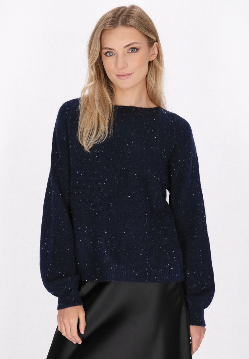 Marineblaues, gestricktes Sweatshirt mit lockerer Passform, das strukturierte Sprenkel und gerippte Bündchen aufweist. Kombiniert mit einem schwarzen Satinkleid.