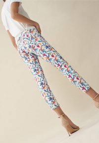 Bílé kalhoty s veselým květinovým vzorem, který obsahuje červené, modré a oranžové listy. Přiléhavý střih, do kotníků, zkombinováno s béžovými lodičkami.