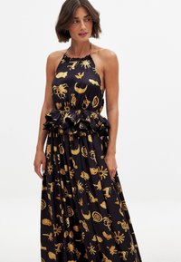 Robe maxi avec un design �à col halter, tissu noir avec des motifs métalliques dorés et une taille froncée. Texture lisse et jupe plissée.