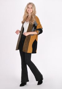 Cardigan lavorato a maglia con un motivo senape, nero e argento; tessuto testurizzato; apertura frontale; maniche lunghe; abbinato a pantaloni neri a zampa.
