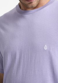 Lavendel bomulds T-shirt med rund hals, korte ærmer og lille hvidt logo broderet på venstre bryst. Glat tekstur.