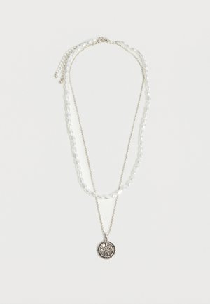 Διπλό κολιέ με μια αλυσίδα από λευκές πέρλες και μια λεπτή ασημένια αλυσίδα που κρατάει ένα στρογγυλό μενταγιόν με ανάγλυφη φιγούρα.