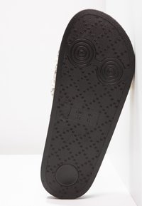 Semelle de chaussure noire avec motif texturé, grips circulaires près des orteils et du talon, et étiquette de taille indiquant EUR 37 US 6.