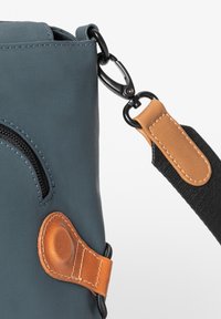 Blauer Nylonbeutel mit schwarzem Zubehör, ausgestattet mit einer Reißverschlusstasche und einem braunen Lederakzent an der Gurtbefestigung.