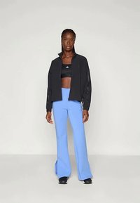 Črna jakna na zadrgo prek črnega kratkega topa in svetlo modrih širokih hlačah. Jakna ima kontrastne detajle in prilegan dizajn.