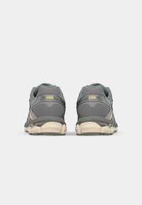 Gray running shoes feature a mesh upper, padded collar, and contrasting yellow detailing. The sole is light beige with a textured finish.