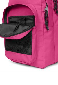 Rosa ryggsäck med en texturerad svart meshpocket, ett blixtlåsfack, och snören för säker förslutning.