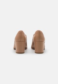 Paire de chaussures beige en cuir à talons carrés, vues de dos sur un fond blanc uni.