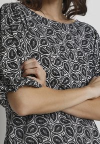 Una persona che indossa un top a maniche puff con un motivo in bianco e nero incrocia le braccia, mostrando un design di tessuto testurizzato.