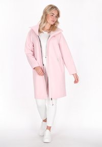 Šviesiai rožinė ilga striukė su aukštu apykakle, užtrauktuku priekyje ir dviem šoniniais kišenėmis. Lygus audinys; dėvima virš baltos palaidinės ir kelnių.