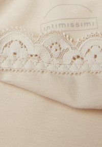 Bežová látka s hladkým povrchem, která zobrazuje složité krajkové lemování na vrchu, s vlnitými okraji a malými kruhovými výřezy.