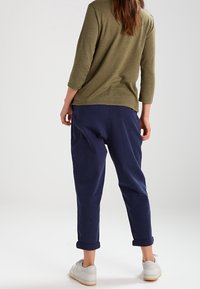 Olijfgroene top met driekwartmouwen, gecombineerd met opgekrulde marineblauwe broeken en lichtgrijze sneakers. Casual materiaal en pasvorm.