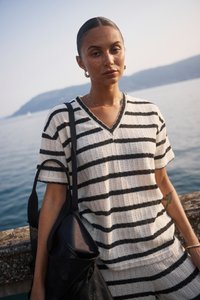 Ribaštruktuuriga kudum valges ja mustas, millel on V-kaelus ja lühikesed varrukad. Kandev must kott, mereäärse taustaga.