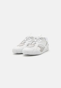Zapatillas blancas que combinan materiales suaves y texturizados, con acentos grises, punta redondeada y un diseño de cordones distintivo.