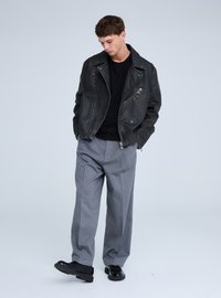 Giacca da motociclista in pelle nera con cerniere argentate, indossata sopra una camicia nera, abbinata a pantaloni sartoriali grigio chiaro e scarpe nere.