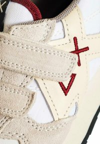 Scarpa da ginnastica bianca con dettagli in suede crema e beige, caratterizzata da ricami rossi e una linguetta in tessuto testurizzato.