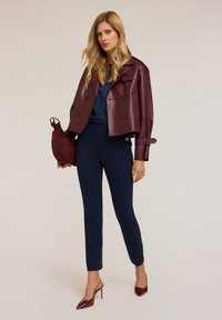 Burgundská zkrácená kožená bunda, navíc modré úzké kalhoty, elegantní burgundské vysoké podpatky a odpovídající kabelka. Hladké materiály s přizpůsobenými designovými prvky.
