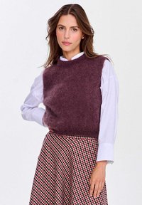 Hedvábný bezrukávový top v tmavě burgundské barvě, s texturovaným povrchem, spárovaný s bílou košilí s límečkem a kostkovanou sukní v růžových odstínech.