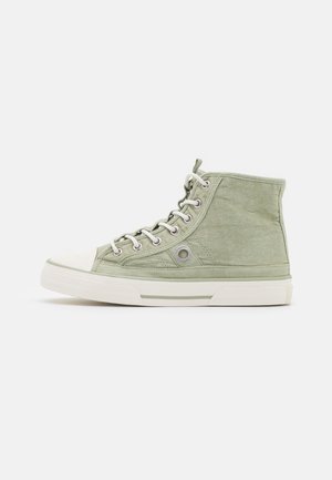 Zapatilla de lona de caña alta en verde claro con suela de goma blanca, puntera blanca y cordones blancos, mostrada de lado sobre un fondo blanco.