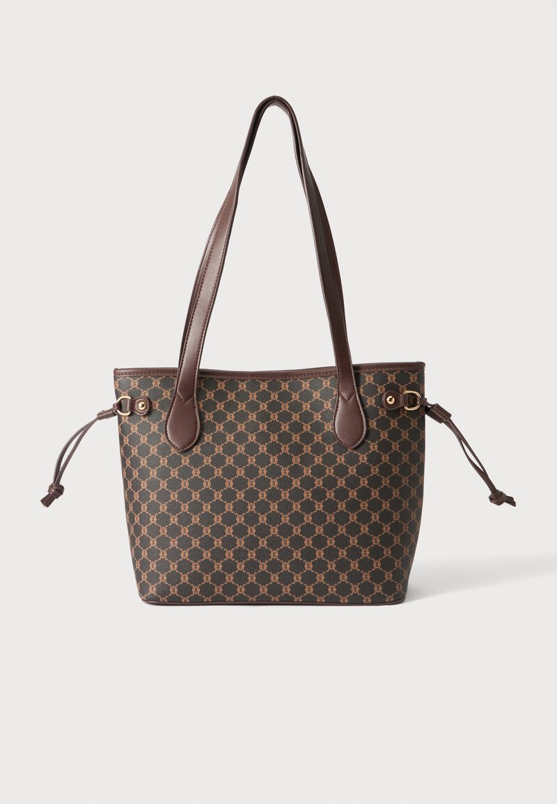 Sac cabas marron avec un motif géométrique répétitif, deux longues anses et des cordons latéraux réglables sur un fond uni.