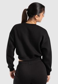 Sweatshirt noir court en tissu doux, avec des manches longues, un col rond, des poignets côtelés et une taille.