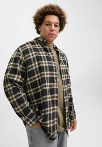 Sort og gul ternet flannel skjorte med lange ærmer og knapkrave, lagd over en grå t-shirt, parret med lyseblå jeans.