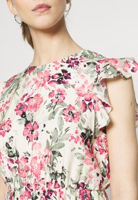 Kukkamekko, jossa on rypytetyt hihat; siinä on vaaleanpunaisia ja valkoisia kukkia vaalealla taustalla; kerroksellinen vyötärö; kevyt kangas.