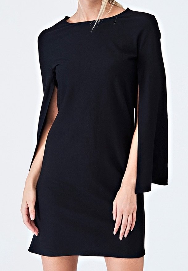 Femme portant une robe noire moulante avec des manches fendues ouvertes, debout devant un fond clair uni.