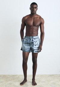 Shorts en denim avec un lavage bleu-gris décoloré, ornés d'un logo blanc sur le côté ; taille élastique et poches latérales, coupe régulière.