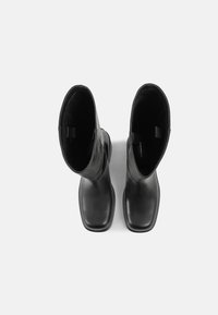 Paire de bottes en cuir noir mi-mollet avec bouts carrés, vues de dessus sur un fond blanc uni.