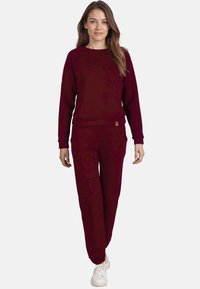 Felpa bordeaux con maniche lunghe e scollo tondo, abbinata a pantaloni della tuta bordeaux. Sneakers bianche completano l'outfit.